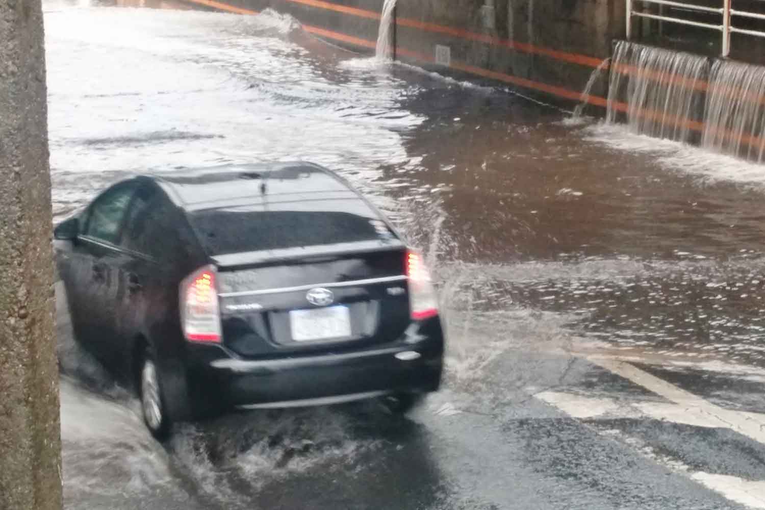 冠水した道路を走る普通自動車のイメージ写真