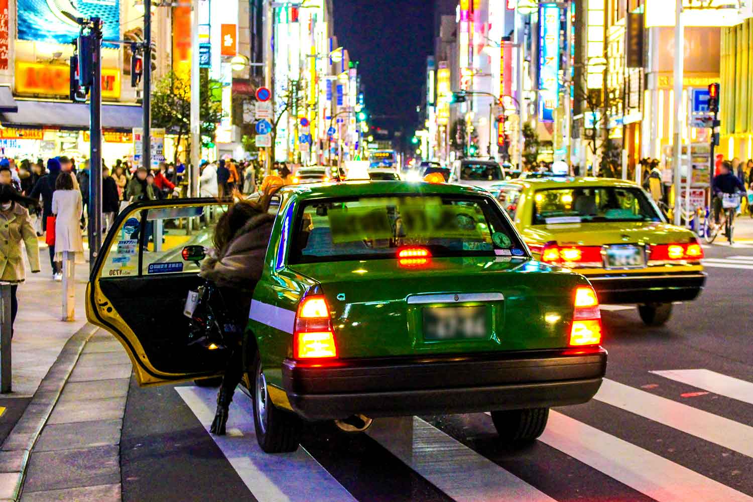 夜の繁華街で乗客を乗せるタクシー