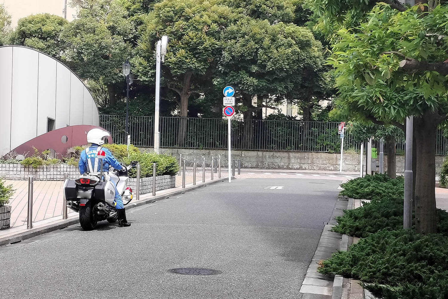 交通違反を取り締まるために建物の影に潜む白バイ隊員